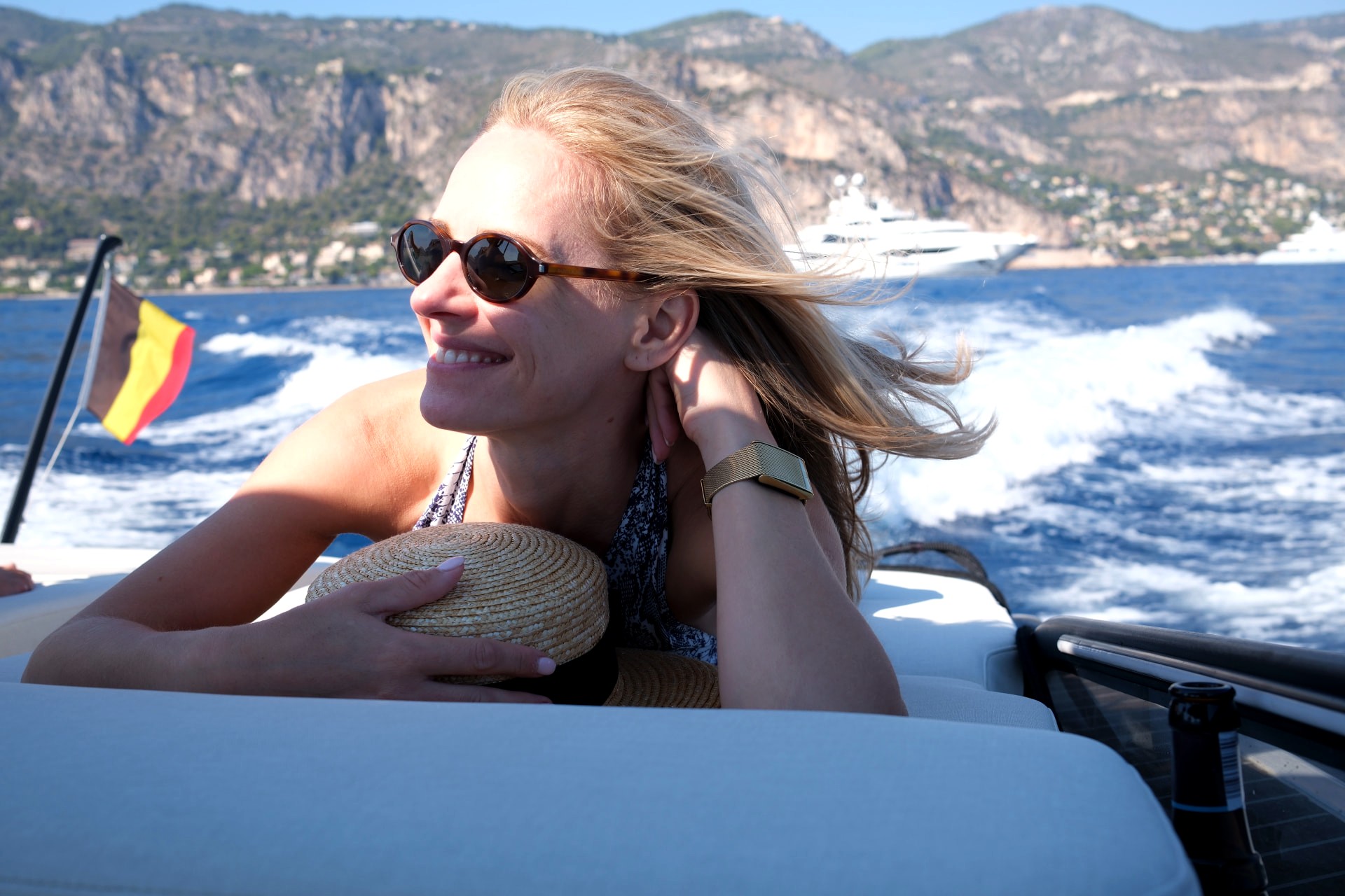 Katarina smiling in the wind at the stern of the B-Craft Akoya, superyachts off the Riviera behind her