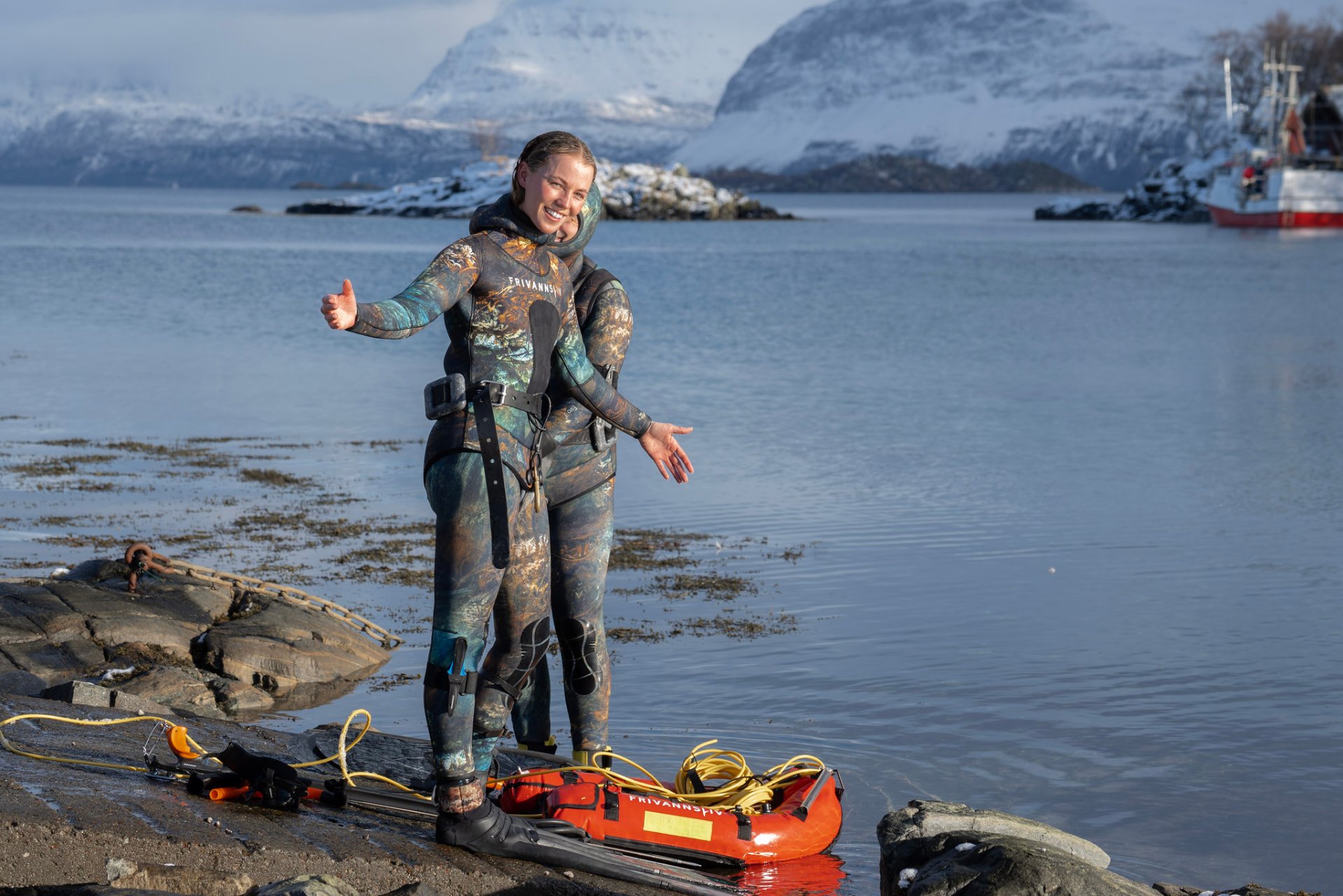 Two freedivers laughing at the water's edge beneath snowy mountains. Photo: Frivannsliv