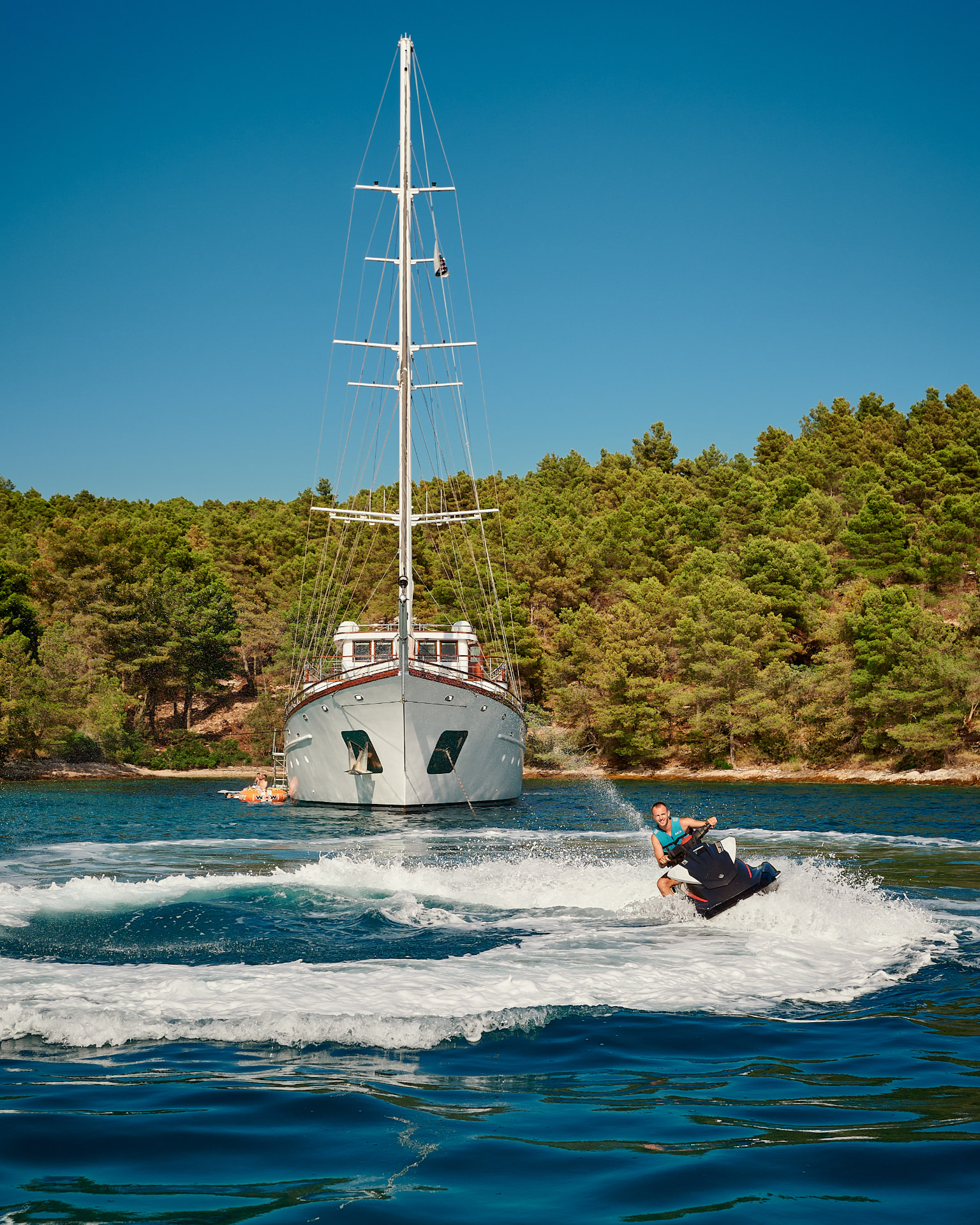 Corsario at anchor with a jet ski carving past her bow