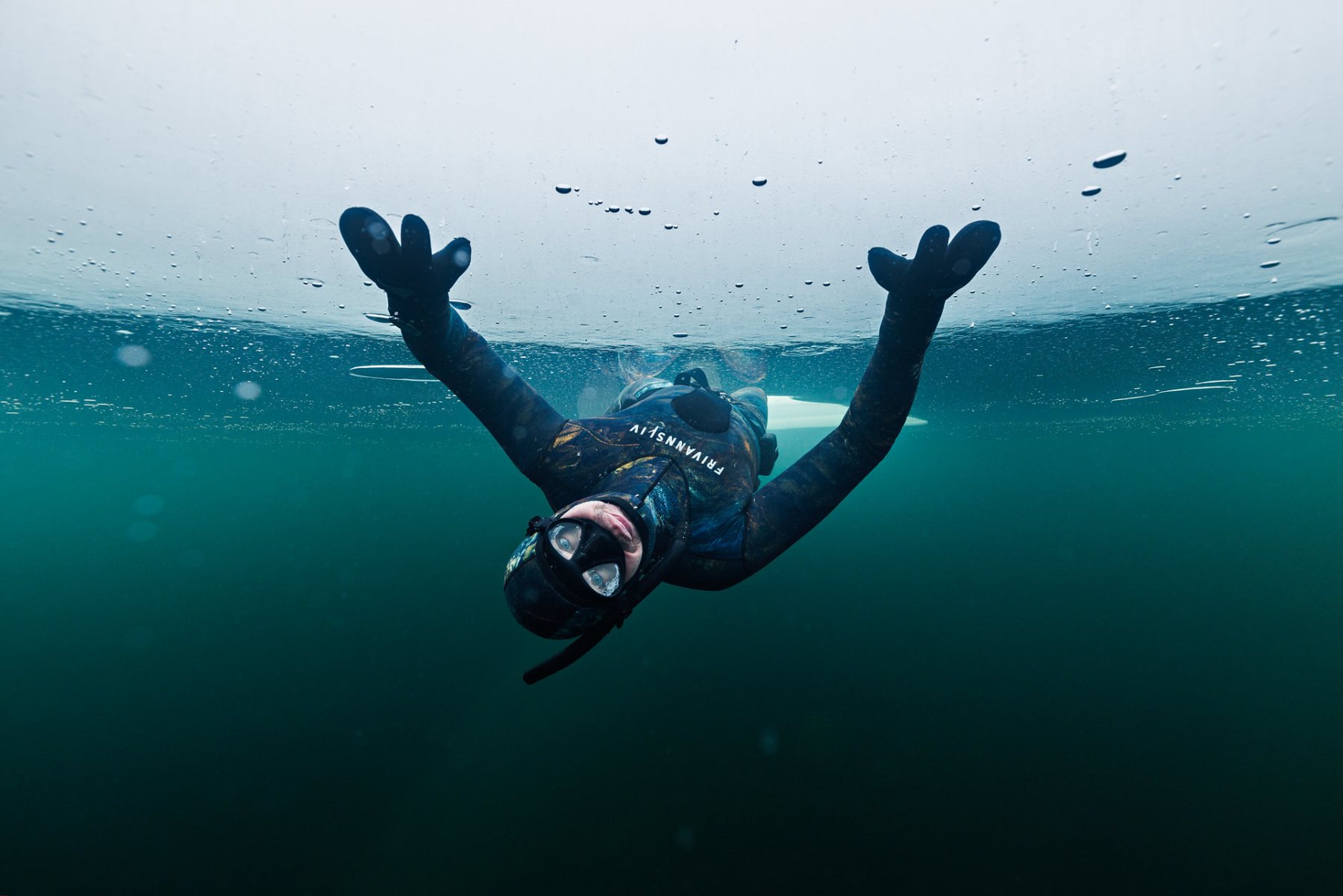 A freediver beneath the ice in clear green water. Photo: Frivannsliv