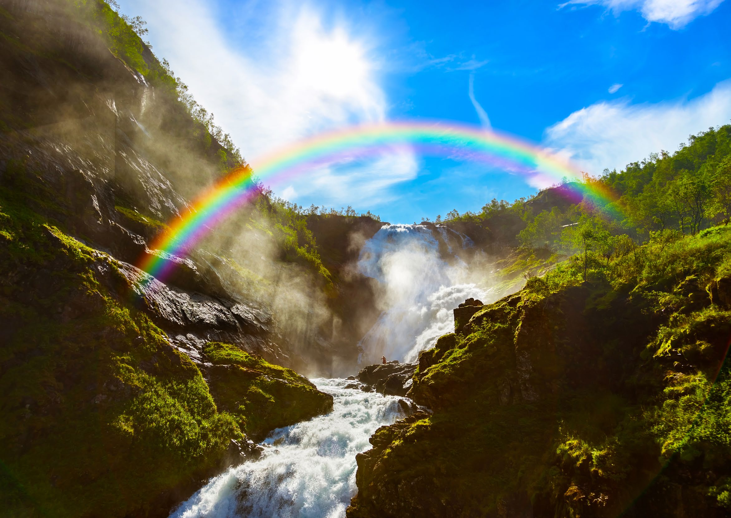 A rainbow over a waterfall tumbling through green rock