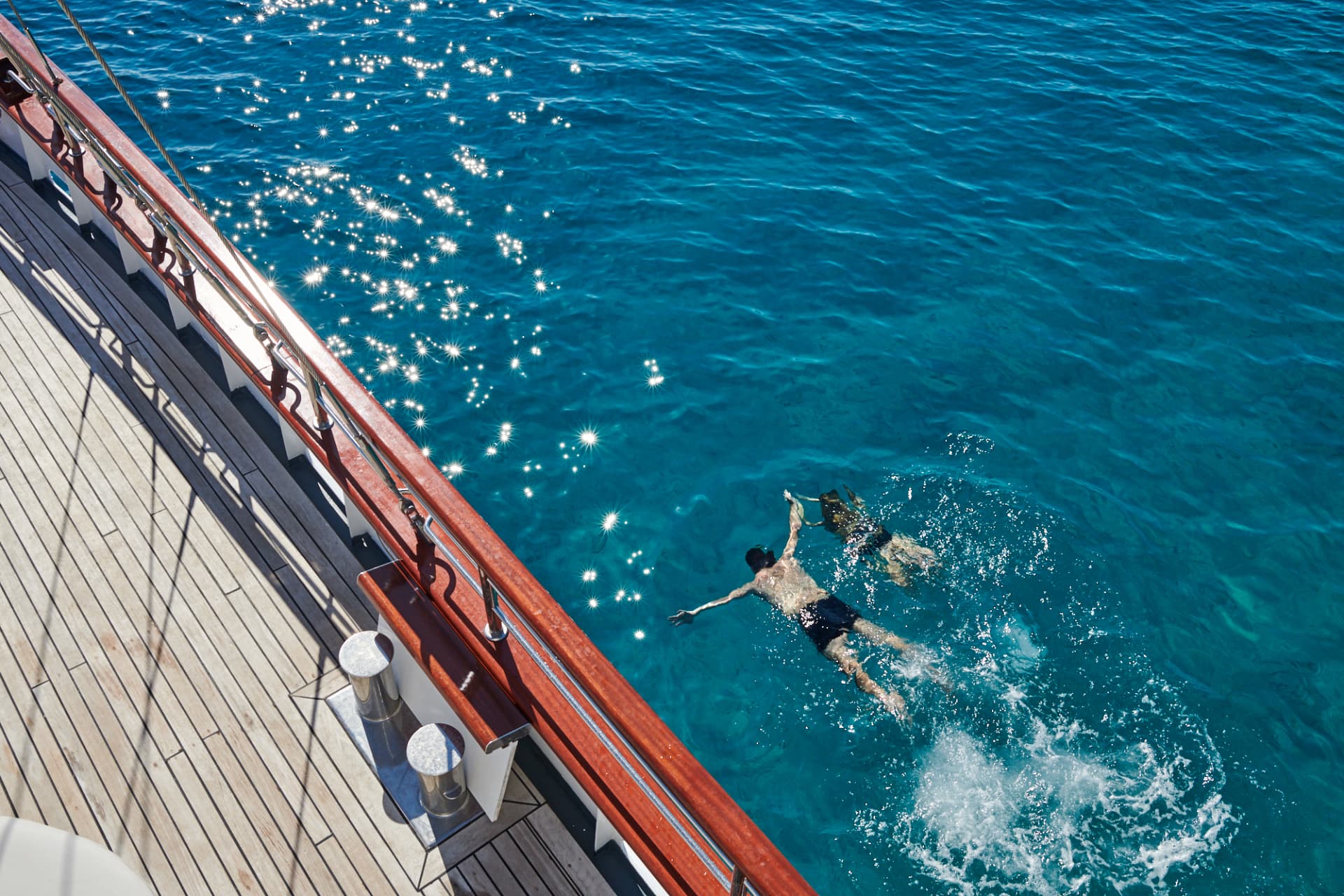 Guests swimming in clear water beside Corsario's teak deck