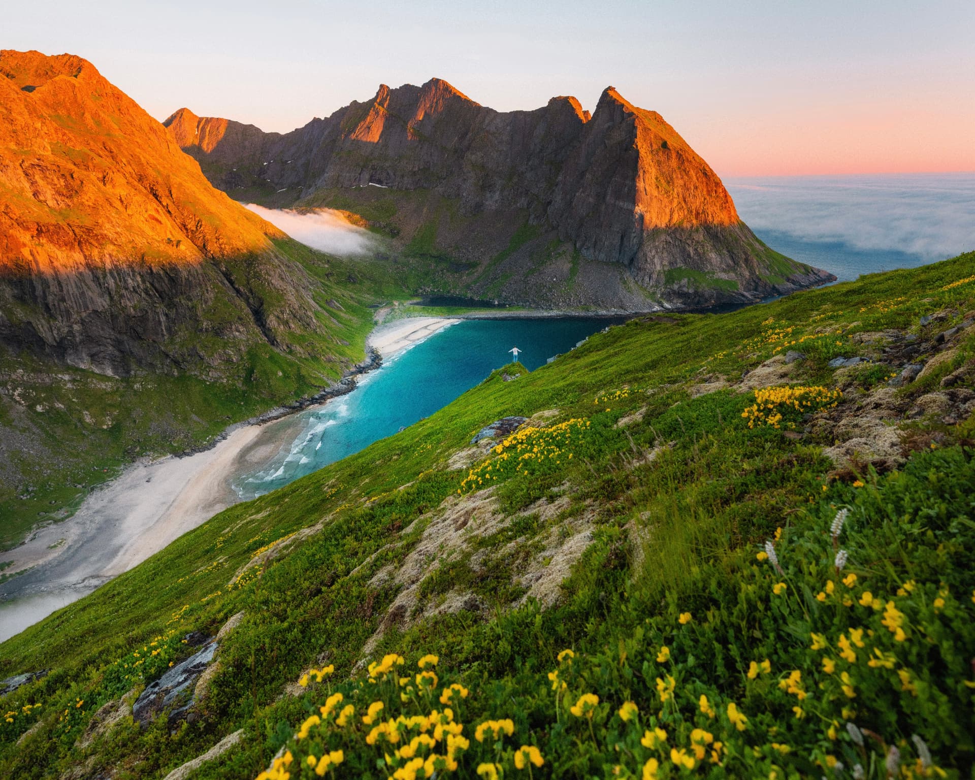 Golden evening light on the Lofoten peaks above Kvalvika's white-sand beach and turquoise water, Norway