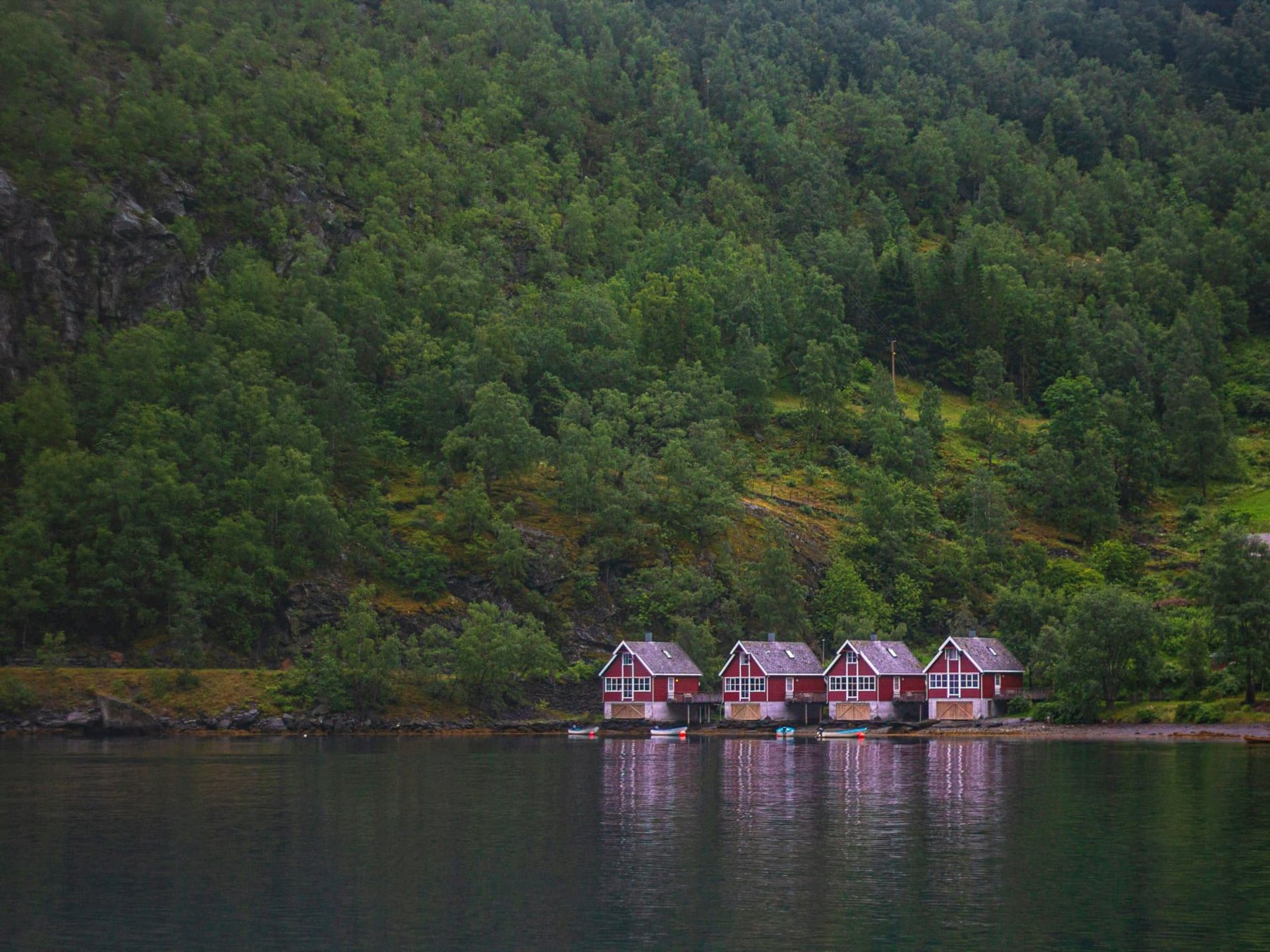 Red wooden boathouses on the shore of a quiet fjord