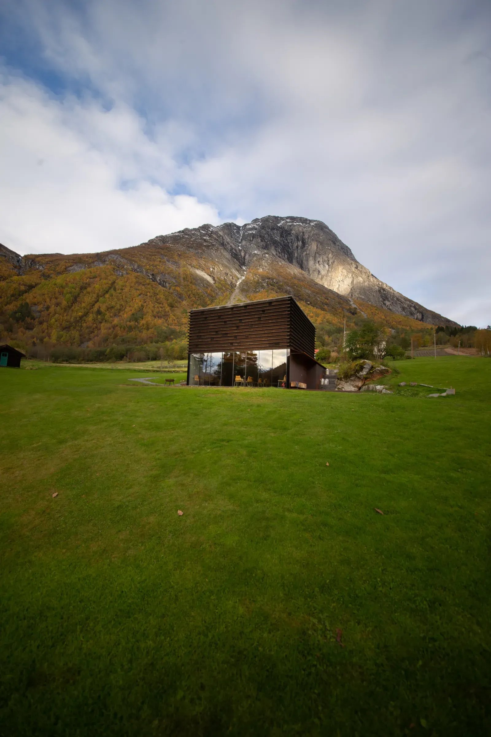 A single Juvet cabin on a green meadow below an autumn mountain. Photo: Juvet Landscape Hotel