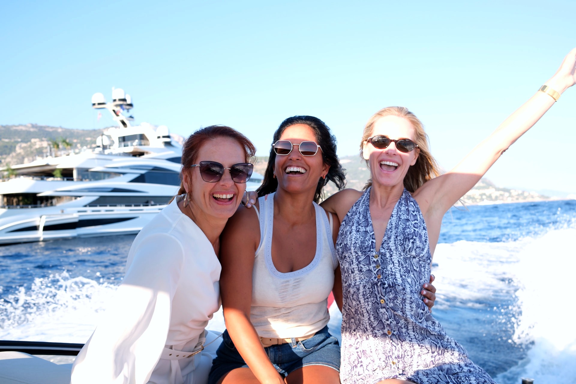 Three friends laughing at the stern of the B-Craft Akoya, a superyacht behind them