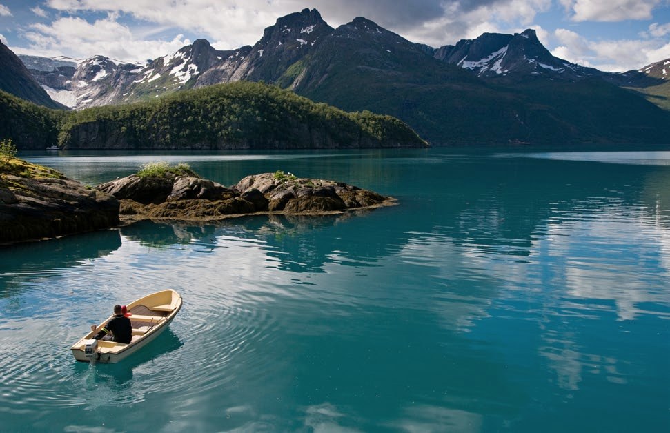 A small boat on still green water below mountains near Finden